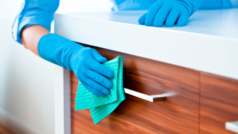 blue hand gloves wearing a hand is cleaning the cabinets using a fibre cloth